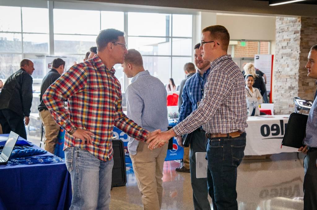 A gentleman at the career shakes hands with an interested student.